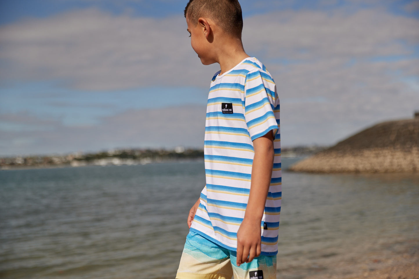 Radicool Kids beach stripe tee: Cotton / spandex tee in white with beach waves printed in horizontal stripes. Radicool Dude badge on chest. We love a stripe, even more when it’s the colours of the beach! Fit is true to size.